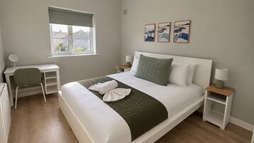 A modern bedroom with a bed, desk, and chair, a window with a view, and artwork on the wall.