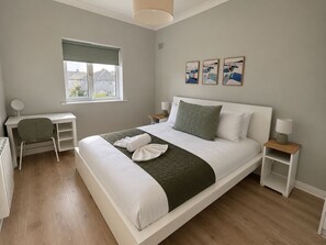 A modern bedroom with a bed, desk, and chair, a window with a view, and artwork on the wall.