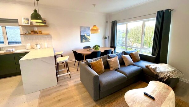 A modern living room with a grey sofa, a coffee table, and a dining area with a table and chairs. - Stylish City Retreat - sleeps 6 (Galway)