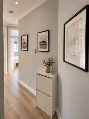 Un couloir avec une armoire blanche, deux tableaux encadrés et une plante en pot.