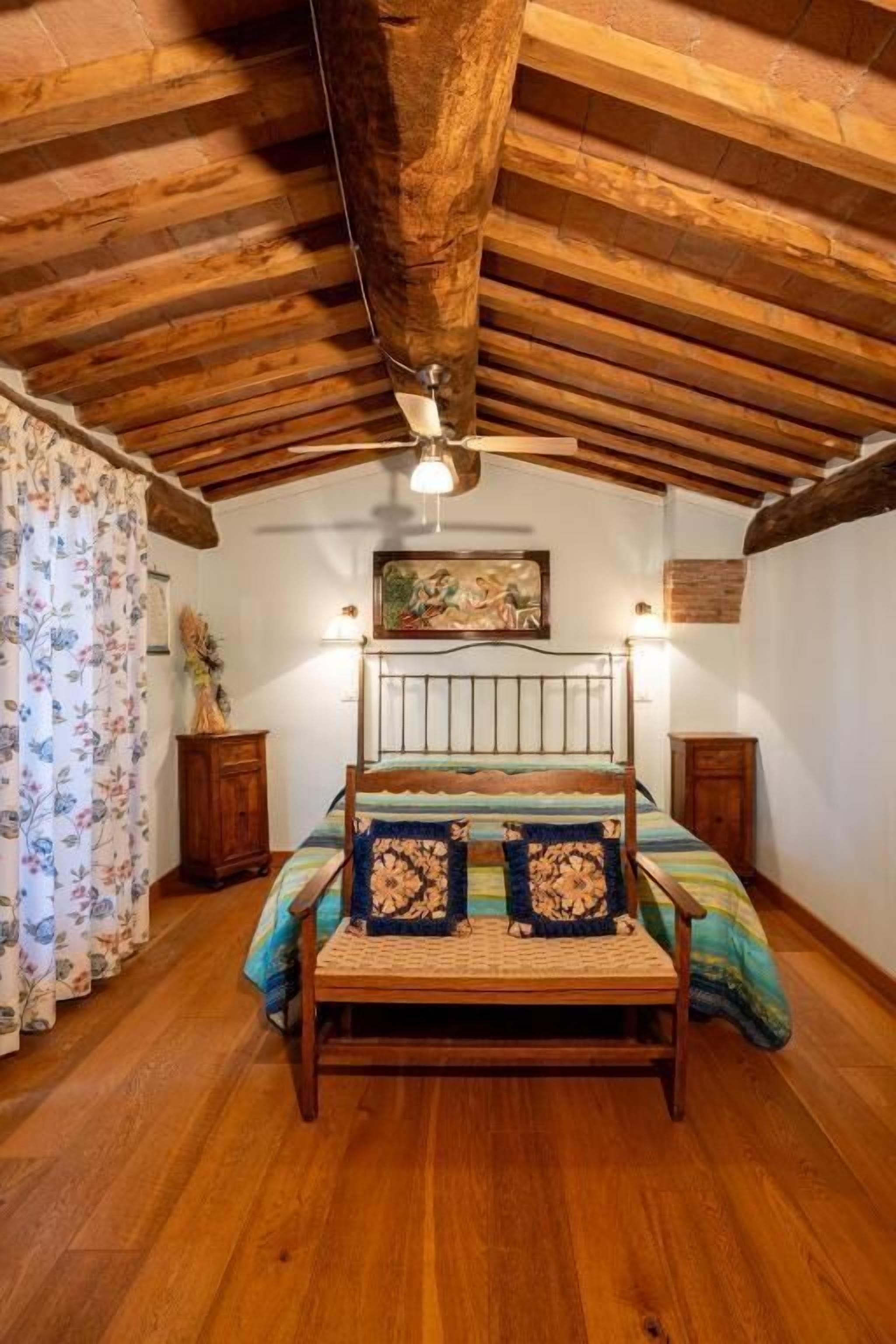 Un dormitorio rústico con techo de madera, una cama con estructura metálica y un cuadro en la pared.