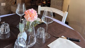 Una mesa de comedor dispuesta con copas de vino y un florero con flores, una chimenea encendida y una pared de piedra.