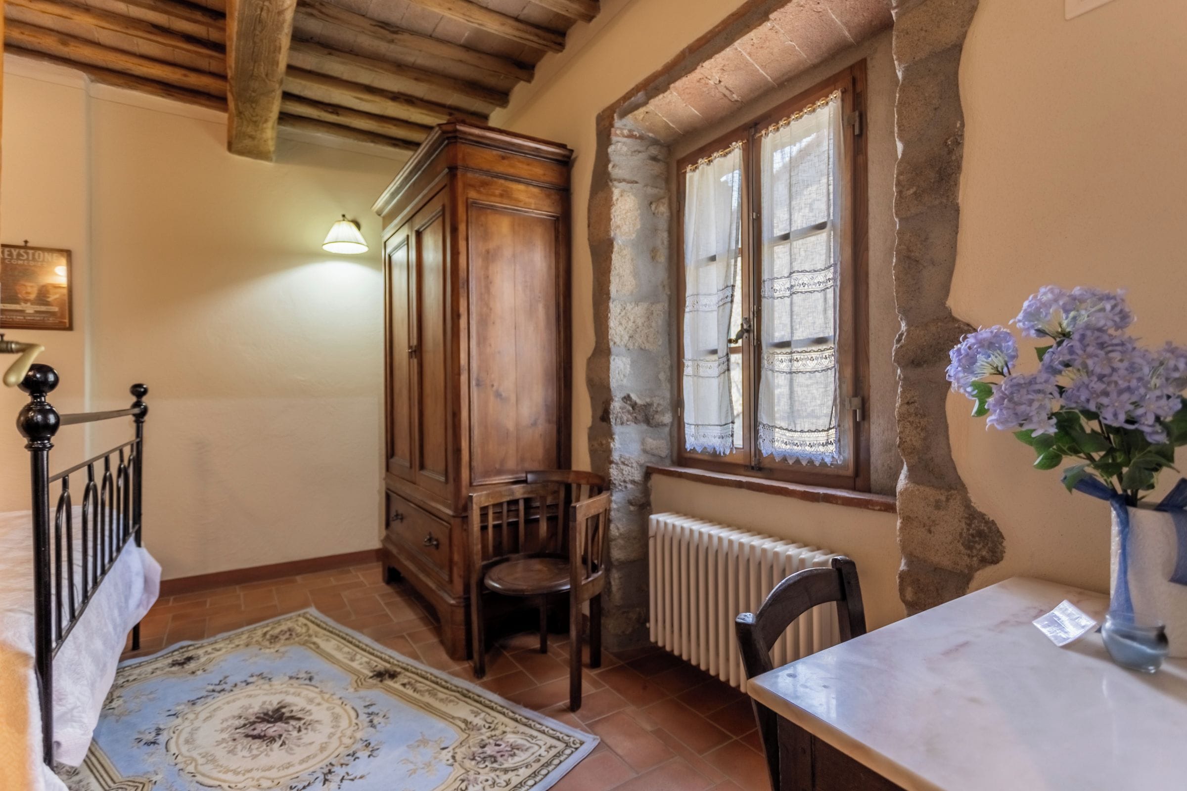 Une pièce avec un meuble en bois, un radiateur, une table ornée d’un vase de fleurs et un tapis à motifs.