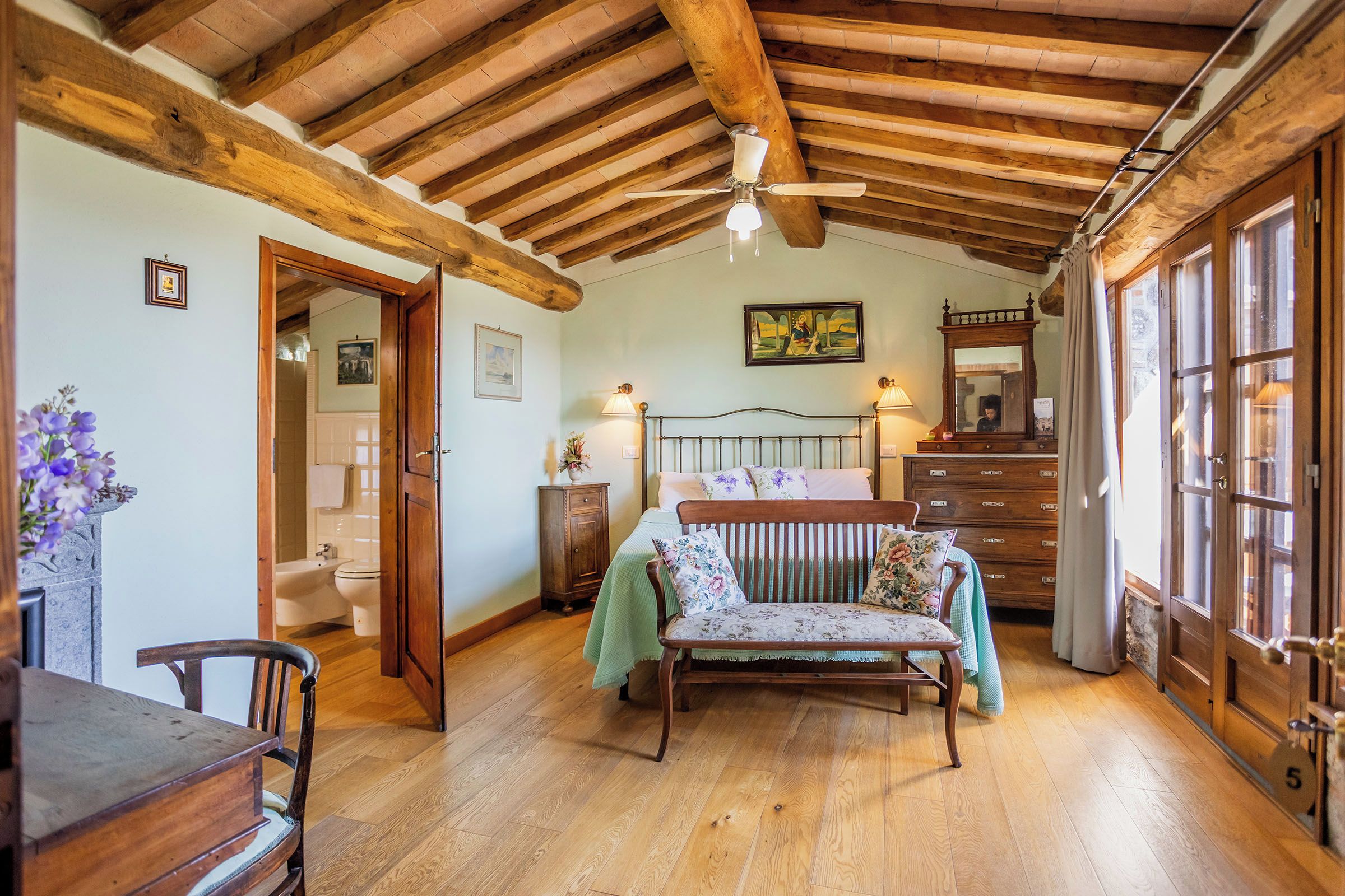 A rustic room with a wooden ceiling, a bed with floral bedding, a wooden dresser, and a window with curtains.