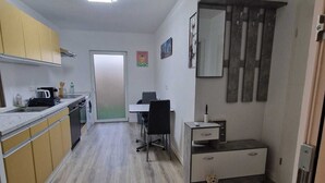 Une cuisine compacte équipée d’un four à micro-ondes, d’un évier et de placards. On y trouve un petit bureau avec une chaise, et un ours en peluche est posé sur le sol.