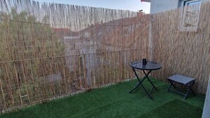 Un jardin avec une pelouse artificielle, une table ronde et un petit banc.