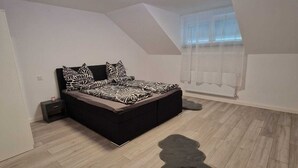 Une chambre à coucher avec un lit, une table de chevet, une fenêtre avec des stores et un luminaire au plafond.