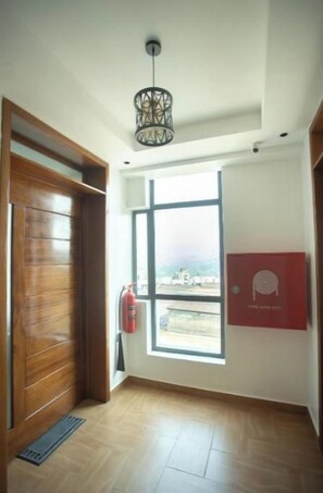 Ein Zimmer mit Holztür, Fenster mit Aussicht, Feuerlöscher und einer Deckenleuchte.