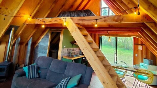 Ein gemütliches Schlafzimmer im Loft-Stil mit einer Holztreppe, einer Sitzecke und Blick ins Freie.