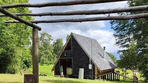 Eine rustikale Holzhütte mit geneigtem Dach, umgeben von einer Wiese und Bäumen.