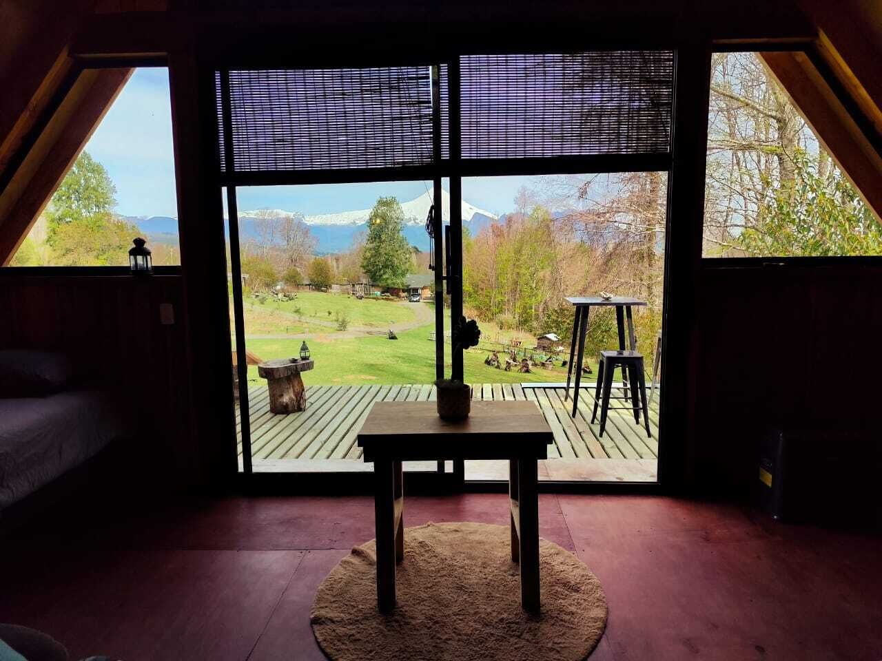 A room with a large window, a wooden table, and a view of a garden and mountains.