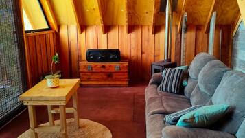 Un interior de cabaña acogedor, con techo de madera, un sofá, una mesa y un aparador.