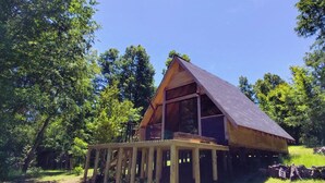 Eine Holzhütte mit geneigtem Dach, einer Terrasse und einem großen Fenster.