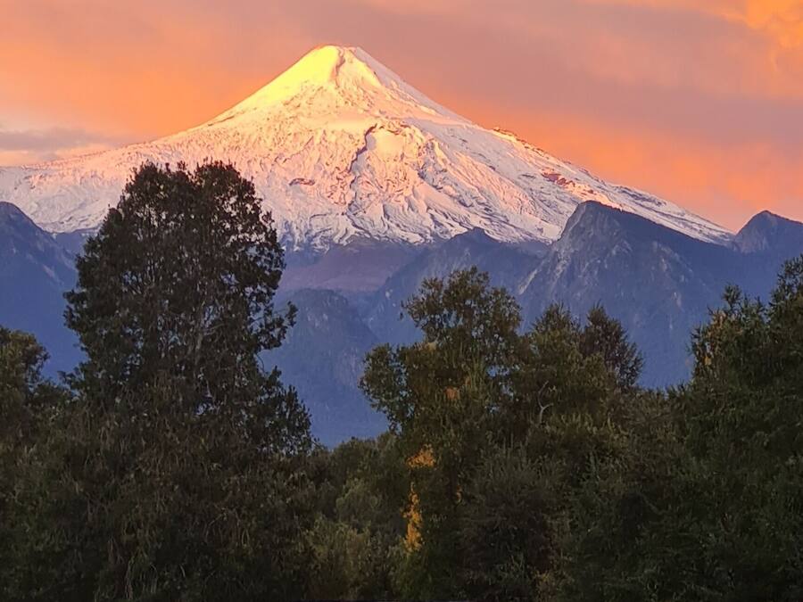 A mountain with a snow-capped peak, a wooden cabin, and a clear sky.