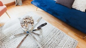 A living room with a blue sofa, a glass coffee table with decorative items, and a remote control on the table. - Stunning House in Heart of Historic Lincoln (Lincolnshire)