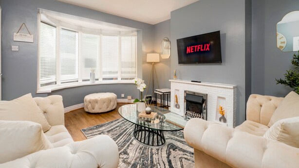 Ein Wohnzimmer mit Kamin, einem an der Wand montierten Fernseher und einem Fenster mit Jalousien.