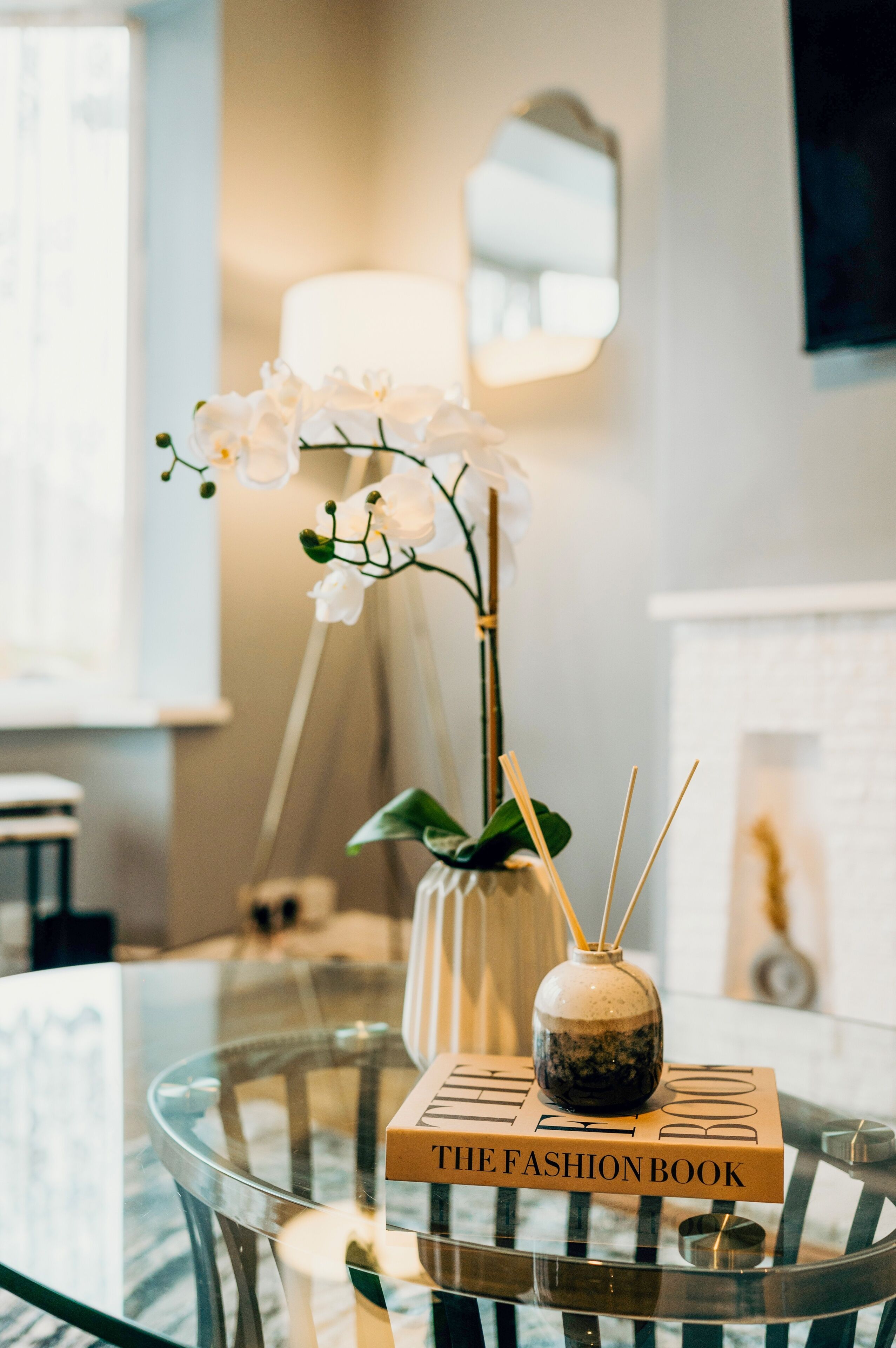 A glass table with a book titled 'THE FASHION BOOK' and a small vase with an orchid.