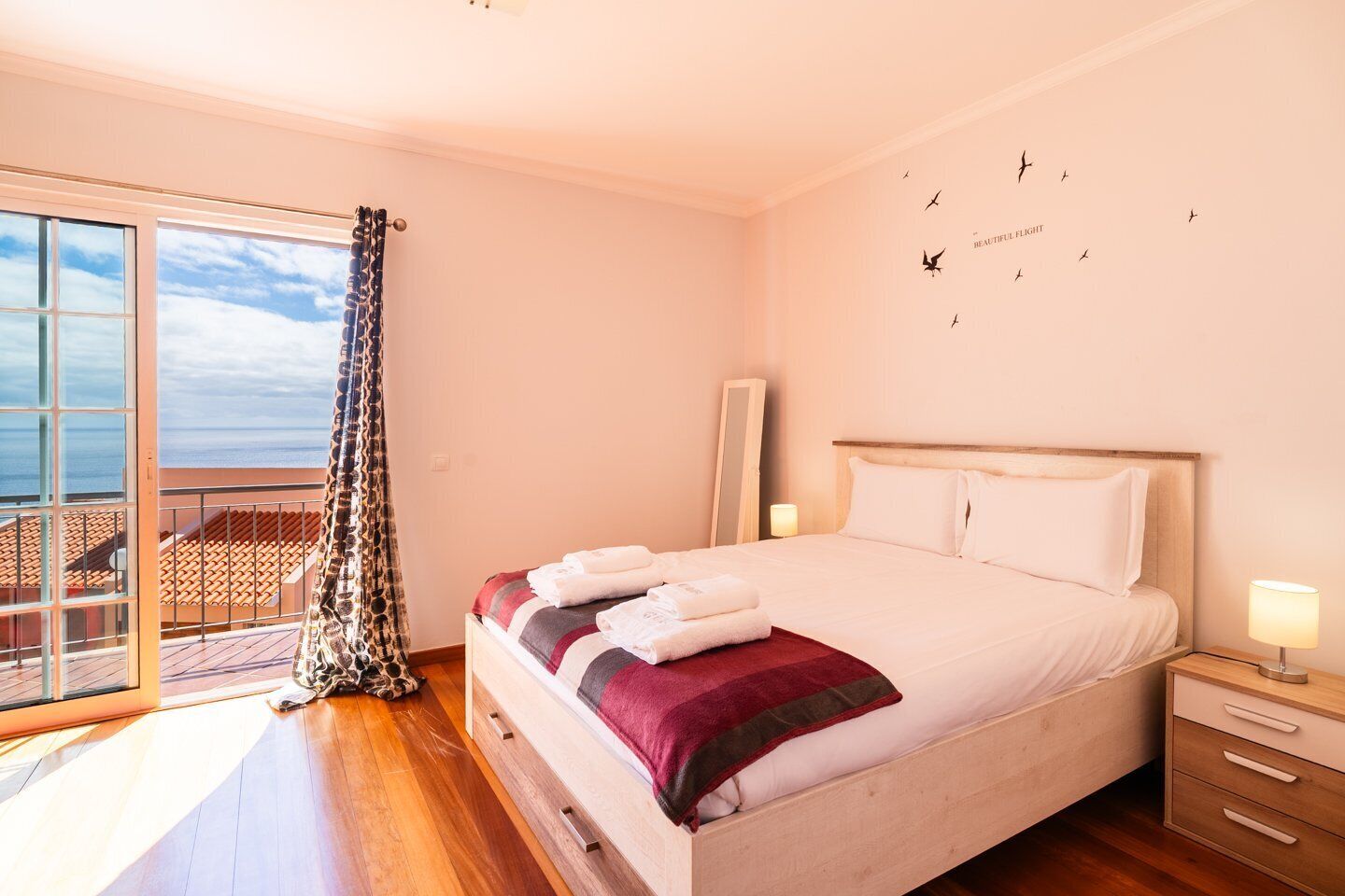 Ein Schlafzimmer mit einem großen Bett, einem Nachttisch, einem Spiegel und Meerblick durch ein Fenster.
