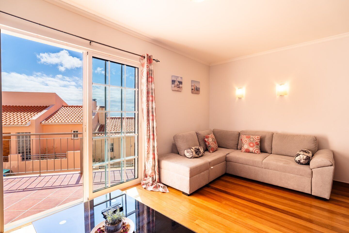 Ein Wohnzimmer mit einem beigefarbenen Sofa, einem Glastisch und einer Glastür, die auf einen Balkon führt.