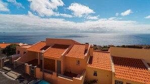 Ett bostadsområde vid kusten med byggnader som har tak av terrakottafärgat material, en klar himmel och utsikt över havet.