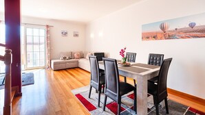 Ett modernt vardagsrum med en matplats, med en soffa, ett matbord med stolar och ett stort fönster med gardiner.