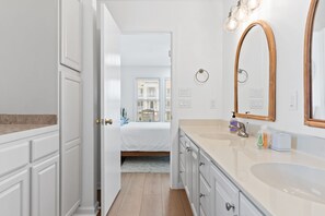 A modern bathroom with a large mirror, a sink, and a bed visible through an open door. - ACCESS TO EVERYTHING! <br>Enjoy comfort, convenience, and elegance during your stay at one of the most sought-after locations on Holden Beach! (Holden Beach)