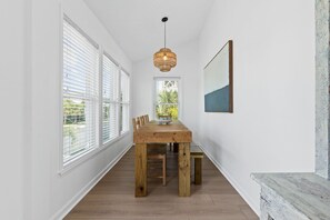 A dining area with a wooden table and chairs, a hanging light fixture, and large windows with blinds. - ACCESS TO EVERYTHING! <br>Enjoy comfort, convenience, and elegance during your stay at one of the most sought-after locations on Holden Beach! (Holden Beach)