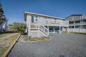 A two-story building with a white exterior, a balcony on the upper floor, and a gravel driveway. - Beautiful Canal front home. Just a short walk to the beach! (Holden Beach)
