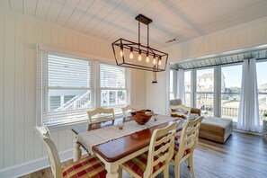 A dining area with a wooden table, white chairs, and a hanging light fixture. - Beautiful Canal front home. Just a short walk to the beach! (Holden Beach)