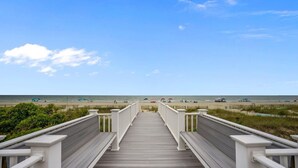 A wooden boardwalk leading to a beach with umbrellas and people in the distance. - The Perfect Oceanfront Vacation w/ Private Pool! (Holden Beach)