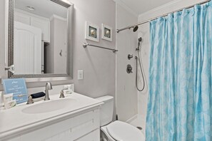 A bathroom with a white sink, a mirror, a shower with a blue curtain, and two framed pictures on the wall.