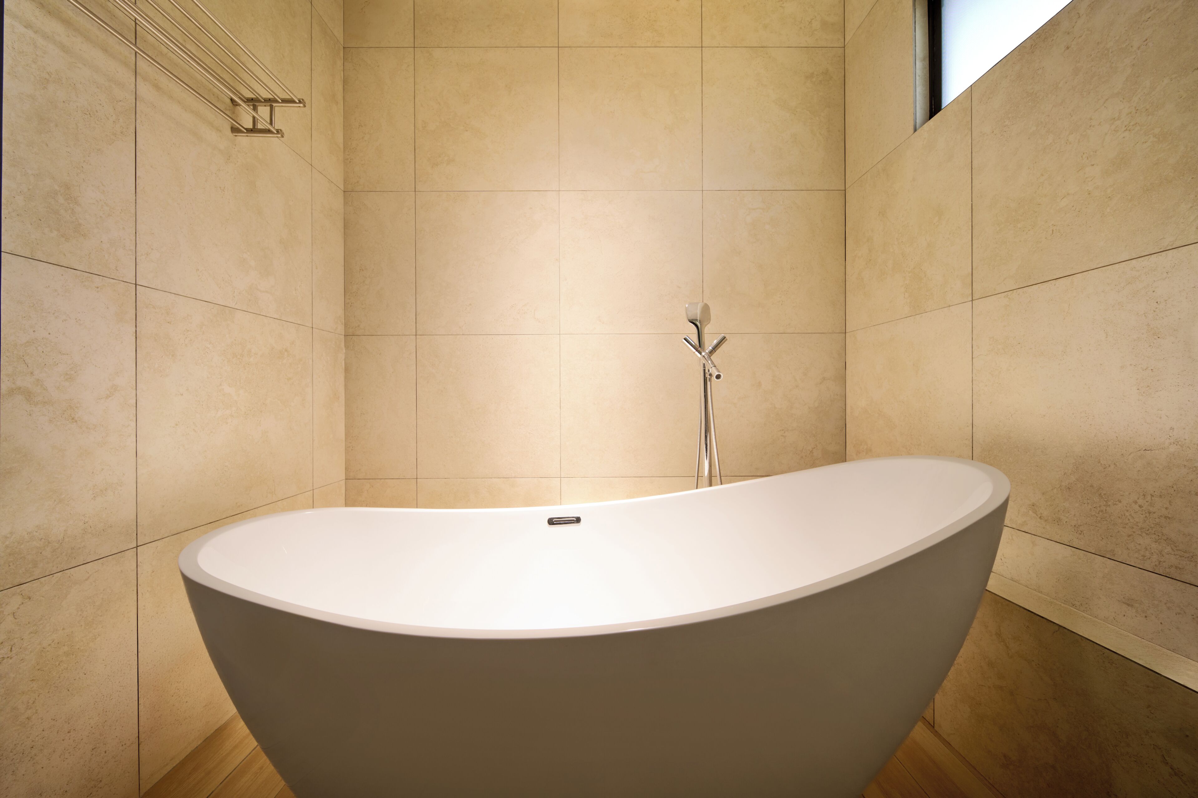 A modern bathroom with a freestanding bathtub, tiled walls, and a window.