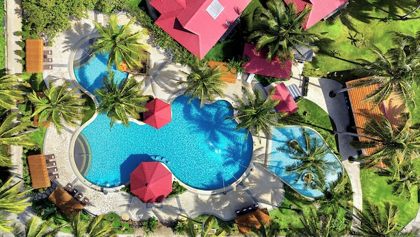 An aerial view of a resort with a large swimming pool, palm trees, and red-roofed buildings. - Hilton Garden Inn Kota Kinabalu Tuaran (Tuaran)