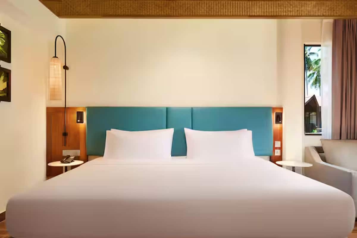 Habitación de hotel con una cama grande, un cabecero verde azulado, una mesita de noche con lámpara y vistas al exterior.