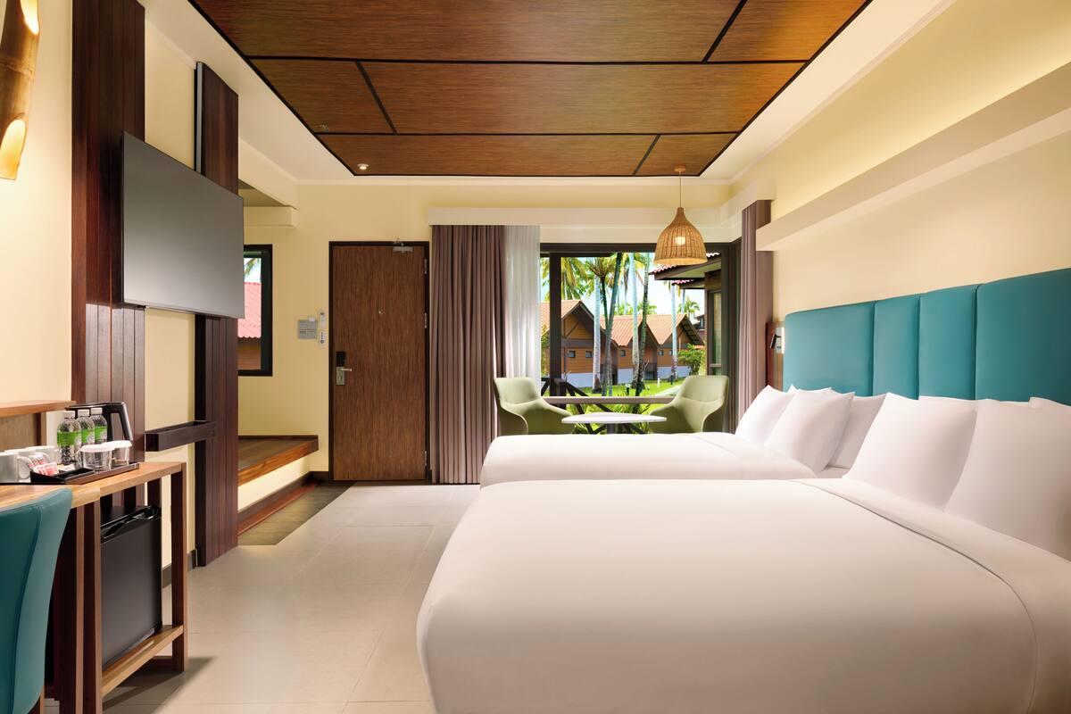 Habitación de hotel con cama, escritorio con refrigerador, comedor con sillas y vistas al exterior.