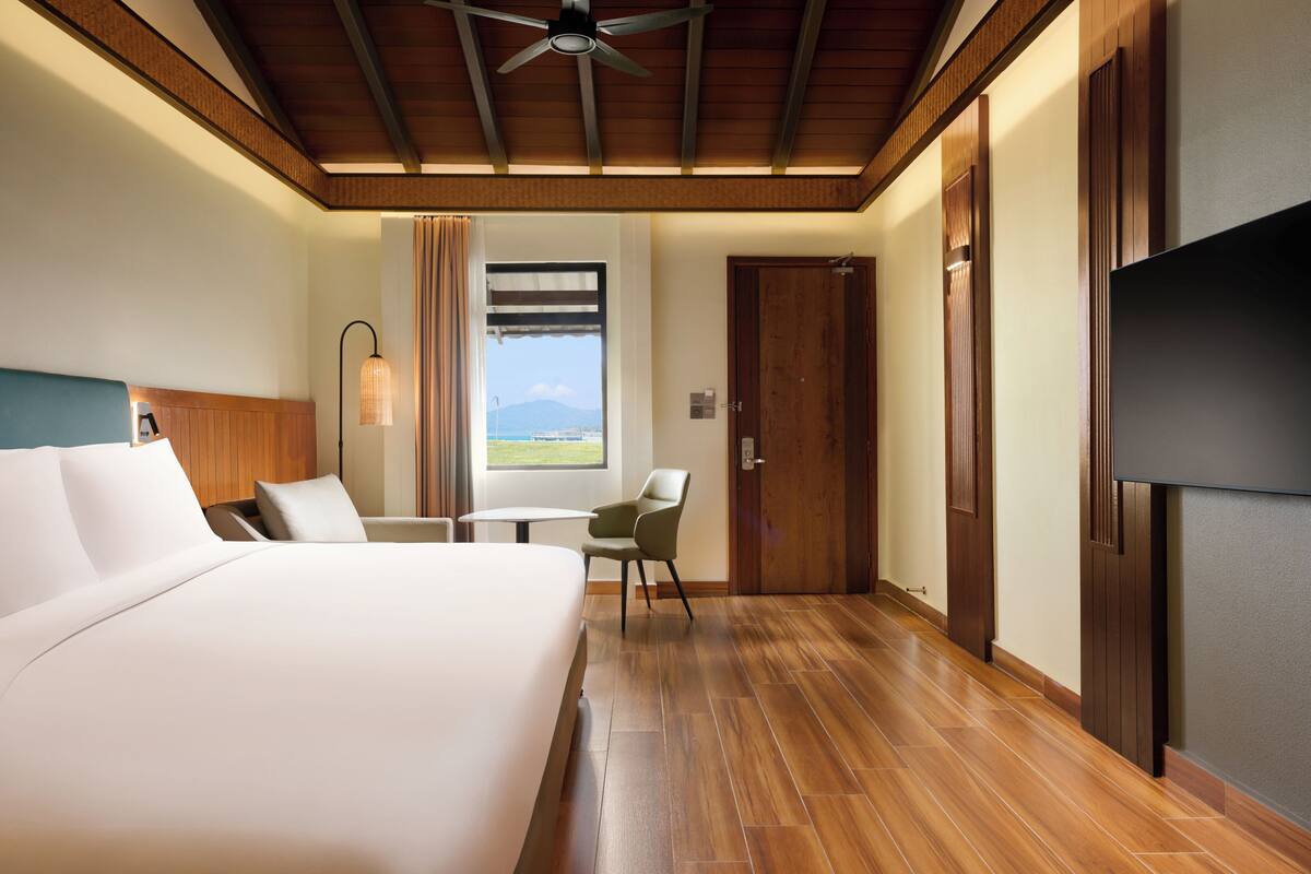 Habitación de hotel con cama, una silla, una mesa, televisor y ventana con vistas.