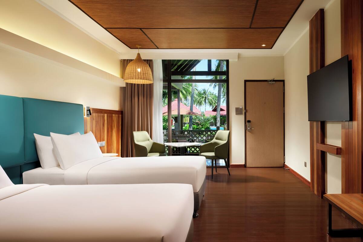 Habitación de hotel con dos camas, televisión, techo de madera y vista al exterior.
