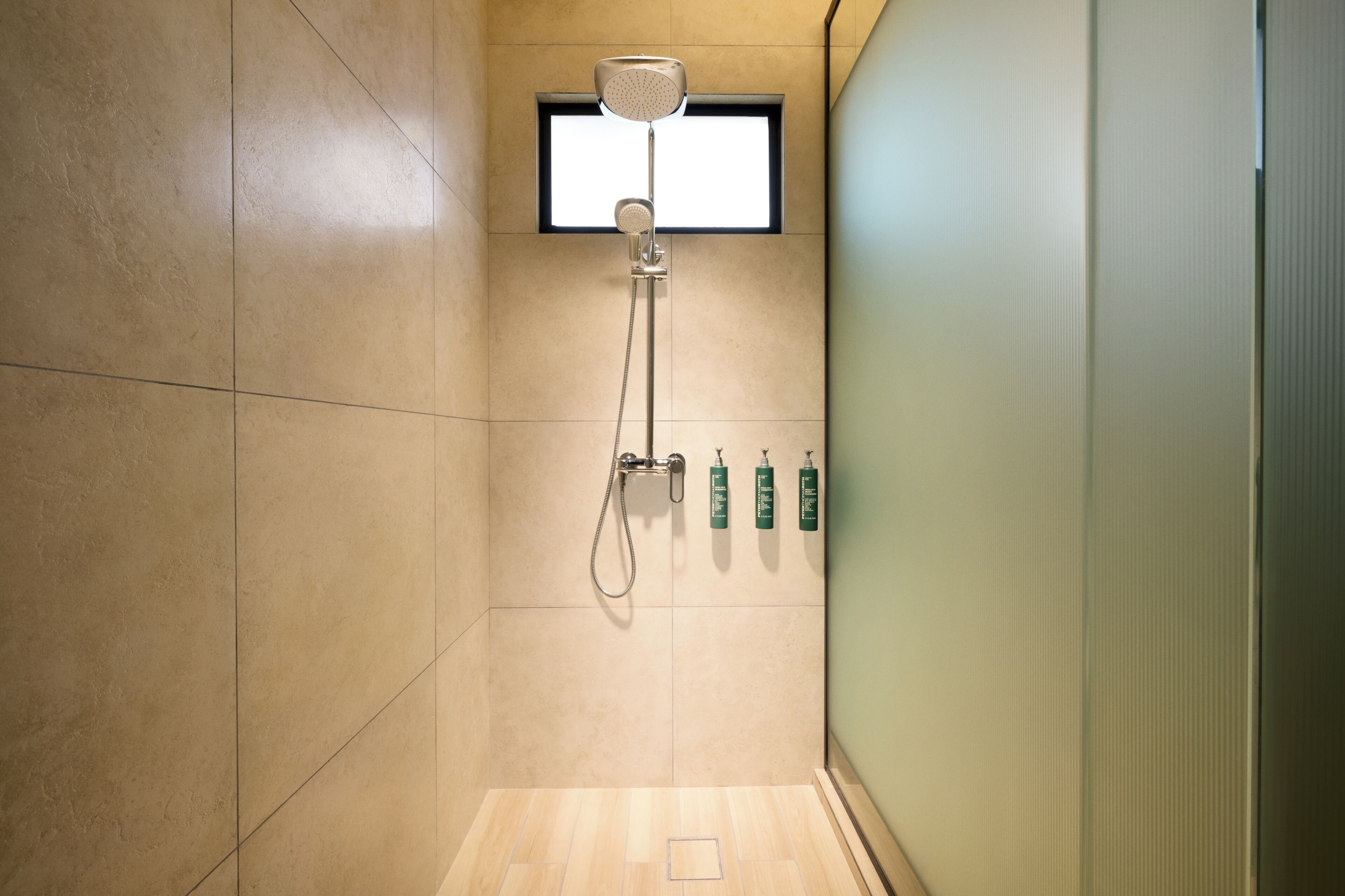 A shower with a handheld showerhead, a window, and a wall-mounted soap dispenser.