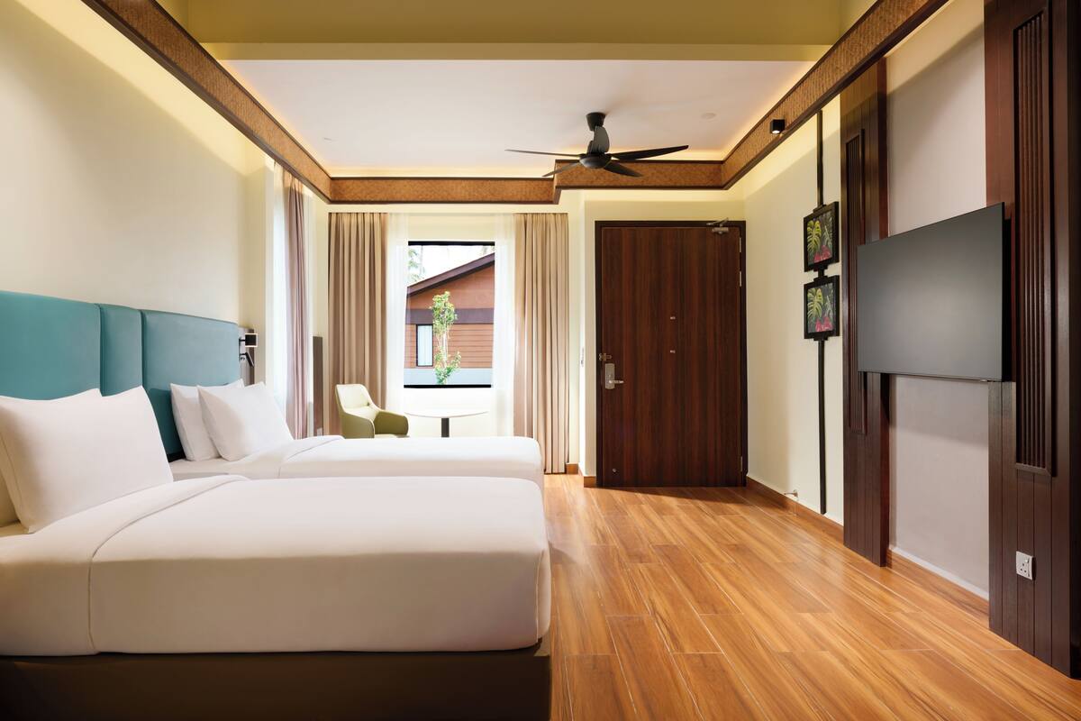 Habitación de hotel con dos camas, ventilador de techo, televisión y vistas al exterior.