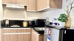A compact kitchen with wooden cabinets, a stainless steel refrigerator, a microwave, and a coffee maker.