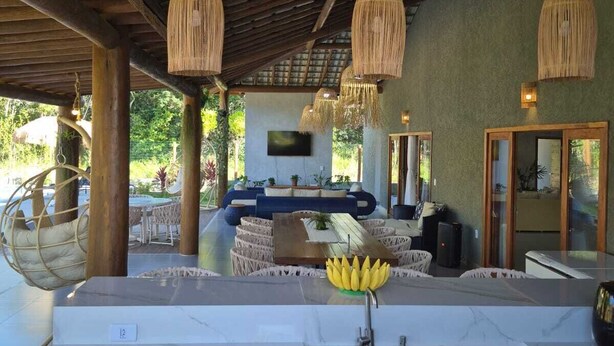 A spacious outdoor area with a wooden ceiling, hanging wicker lamps, a seating area with cushions, and a central table with a banana. - Beach house in Arraial d`juda Bahia, close to the best beaches in the region. (Arraial d'Ajuda)