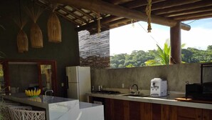 A modern kitchen with a white island, wooden cabinets, and a view of lush greenery. - Beach house in Arraial d`juda Bahia, close to the best beaches in the region. (Arraial d'Ajuda)