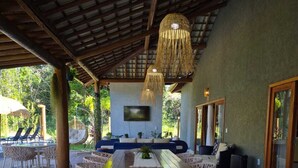 A covered outdoor seating area with a thatched ceiling, a central table, and a decorative sunflower arrangement. - Beach house in Arraial d`juda Bahia, close to the best beaches in the region. (Arraial d'Ajuda)