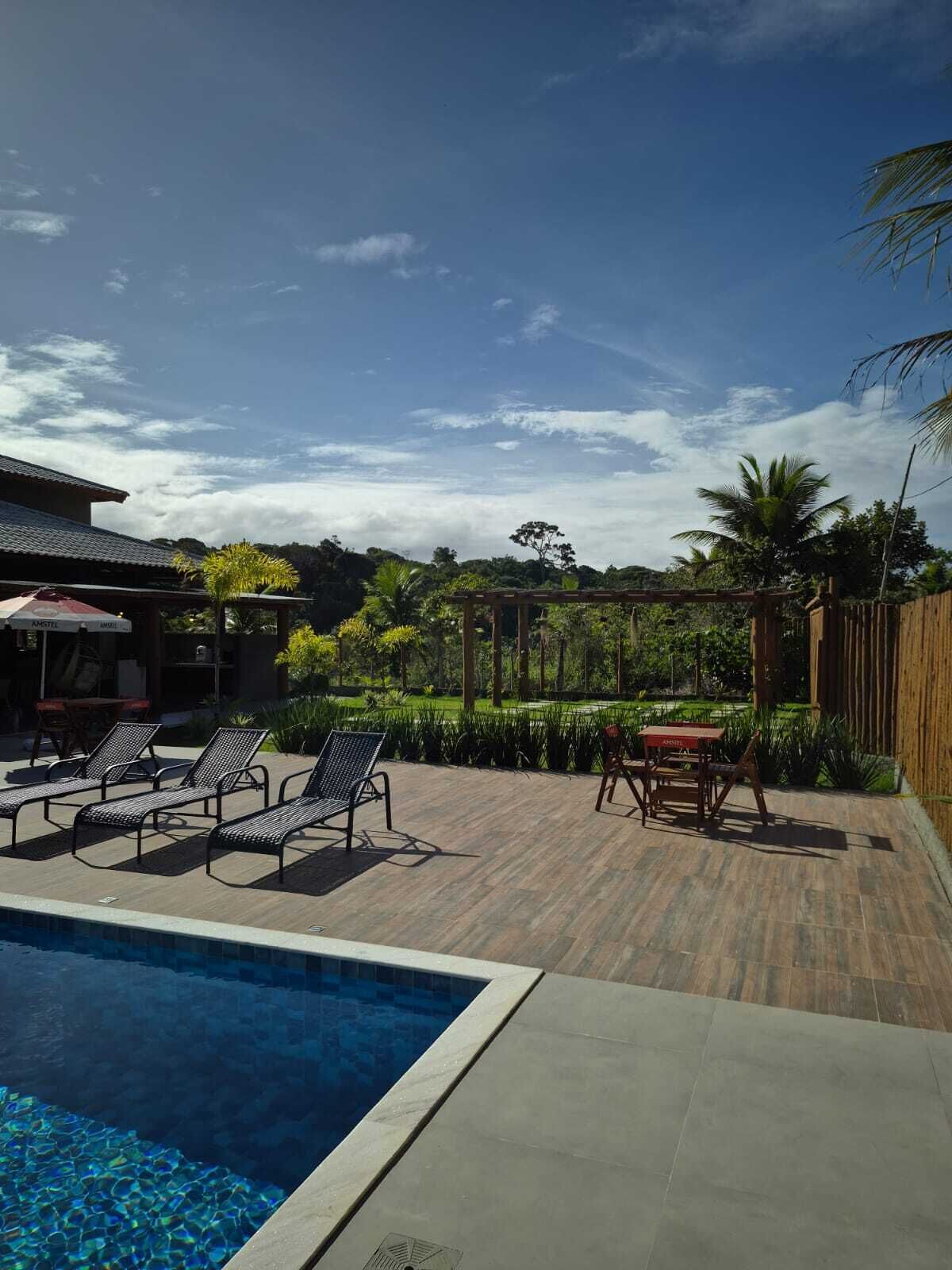 A pool area with lounge chairs and a table, surrounded by a wooden deck and lush greenery.
