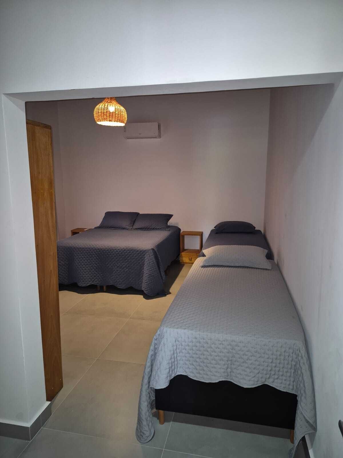 A small, well-lit bedroom with two beds, a wooden wardrobe, and a hanging light fixture.
