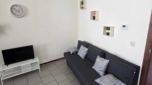 A living room with a black sofa, a white TV stand, a clock, and three small wall-mounted planters. - Maison du Beffroi de Mons (town center) (Mons)