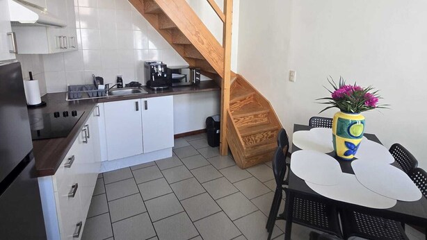 A compact kitchen with white cabinets, a wooden staircase, and a dining area with a table and chairs. - Maison du Beffroi de Mons (town center) (Mons)