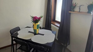 A dining area with a table and four chairs, a vase with flowers, and a window with curtains. - Maison du Beffroi de Mons (town center) (Mons)