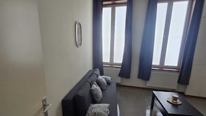 A living room with a sofa, a coffee table, and a window with curtains. - Maison du Beffroi de Mons (town center) (Mons)