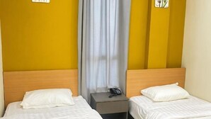 Une chambre d’hôtel avec deux lits, une table de chevet avec un téléphone et un rideau.